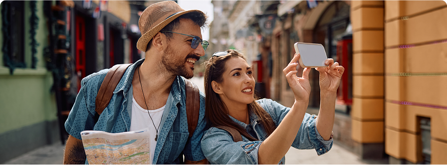 Two tourists on a city street taking photos with a smartphone, staying connected internationally with XeSIM prepaid travel esIM data plan.