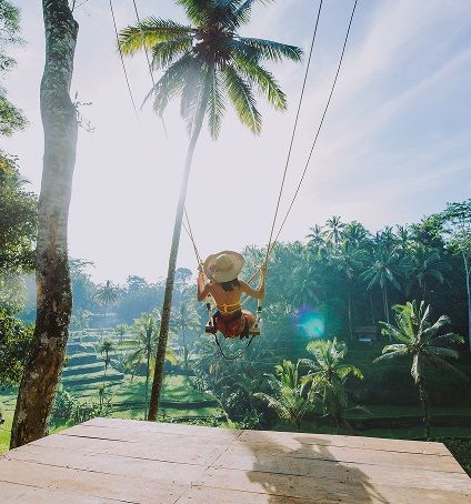 Person swinging between palm trees above lush tropical greenery and terraced fields, reflecting XeSIM's eco-conscious travel vision.